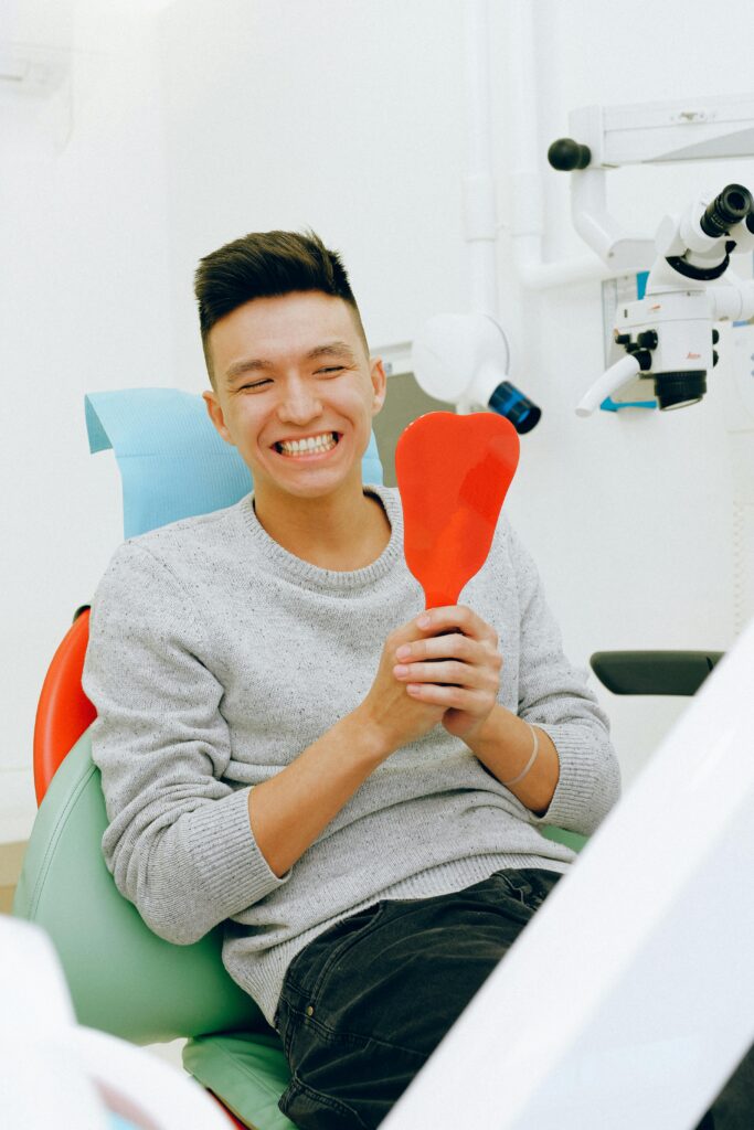 pexels-photo-3845843-3845843 Smiling man holding a mirror during a dental checkup in a clinic setting.